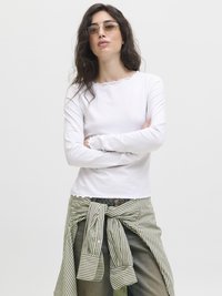 Hvit langermet topp med en bølget hals, kombinert med en grønn og hvit stripete skjorte knyttet rundt livet over denimbukser.