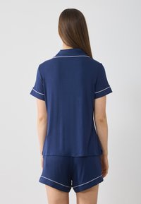 Marins blått pyjamasset i mjukt tyg, med en kragad t-shirt med kort ärm och vit infälld kant samt matchande shorts med rullade fållar.