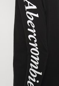 Zwarte sweatshirt met lange mouwen, voorzien van het woord "Abercrombie" in grote witte letters langs de rechter mouw. Glad stoftextuur.