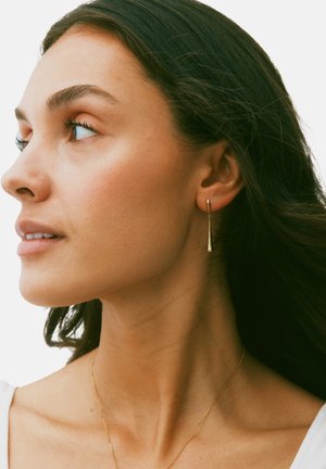 Kuldsetest ripatsest kõrvarõngastest, millel on kitsenev disain, mis ripub just allpool kõrvakõhre, omades poleeritud pinda ja õrna läiget.