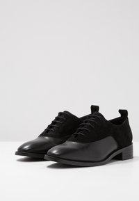 Chaussures oxford noires avec un bout en cuir lisse et un dessus en daim texturé. Design à lacets avec un petit talon empilé pour la stabilité.