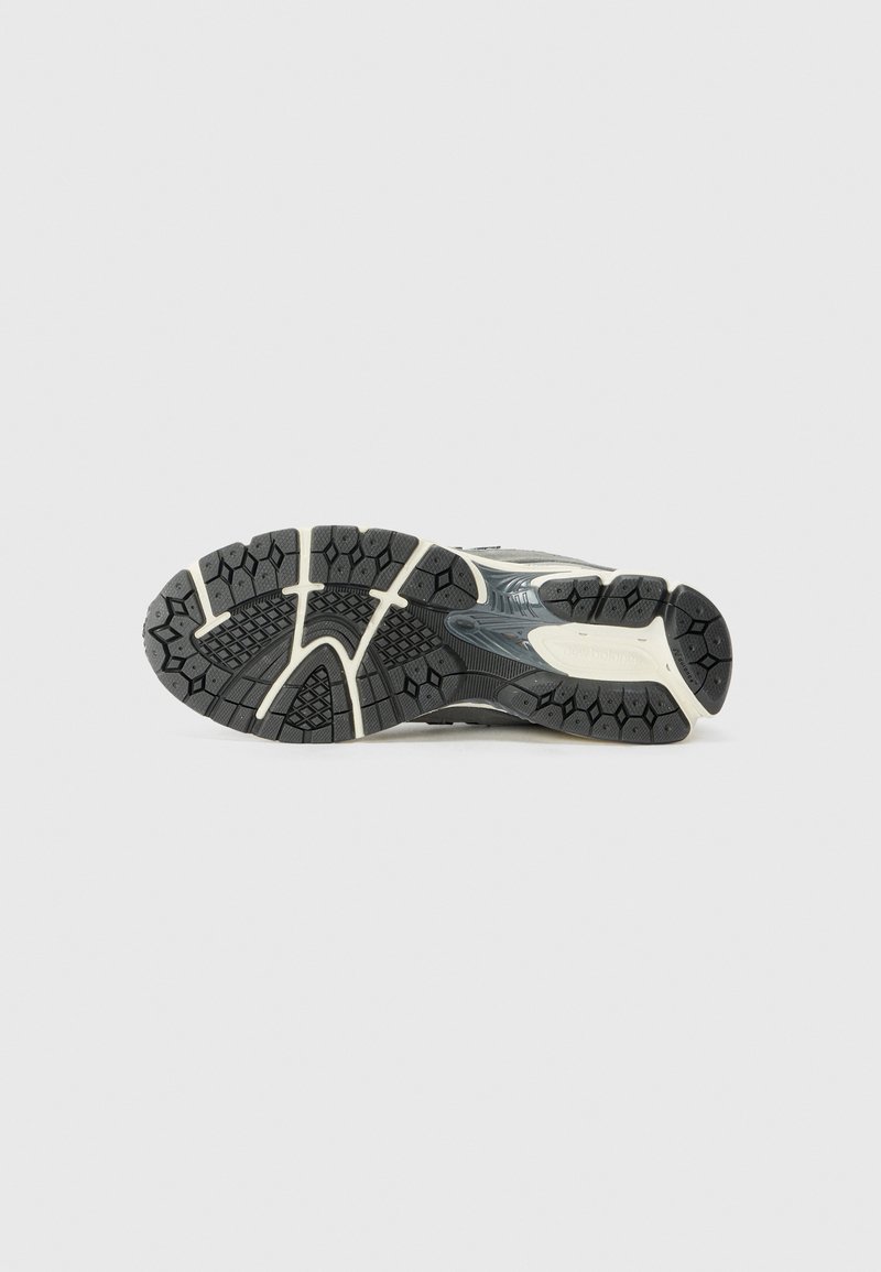 Suela de zapato deportivo en negro y gris con patrones texturizados, que presenta una banda de rodadura de goma para agarre y estabilidad, y una sección central suave.