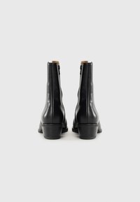 Stivaletti in pelle nera con punta rotonda, zip laterale e tacco a blocco di 5 cm; texture liscia con dettagli di cucitura sottili.