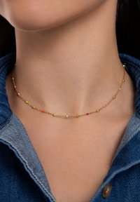 Collana d'oro con piccoli e colorati perline rosa, blu, giallo e arancione, con accenti dorati arrotondati, indossata sulla pelle.