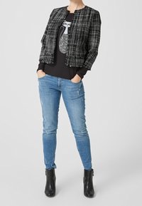 Mustavalkoinen ruudullinen takki lyhyellä mallilla mustan t-paidan päällä, jossa on kissagrafiikka. Asusteena siniset kuluneet farkut ja nilkkurit.