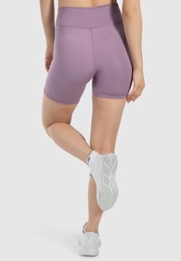 Lila, wysokie spodenki sportowe, gładka faktura, bezszwowy design, w połączeniu z białymi butami sportowymi z fakturowaną podeszwą.
