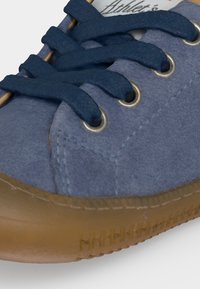 Baskets en daim bleu avec lacets bleu marine et semelle en caoutchouc marron, gros plan montrant la zone des orteils et les œillets métalliques.