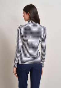 Langärmliges Turtleneck-Shirt in Marineblau mit weißen Streifen, mit einer figurbetonten Passform und einem weichen, elastischen Stoff. Getragen mit dunklen Denim-Jeans.
