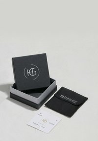 Schmuckbox in Schwarz mit silbernem Logo, grauem Innenfutter und einem kleinen schwarzen Beutel mit der Aufschrift "HAZE & GLORY." Enthält ein weißes Etikett.