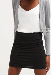 Svart rynkad minikjol kombinerad med en vit V-ringad topp och en grå cardigan. Den har mjukt tyg och en figurnära design.