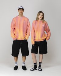 Zwei Models tragen übergroße, verlaufende Pullover in Rosa und Orange, kombiniert mit schwarzen Shorts. Die Accessoires bestehen aus Kappen und Sandalen.