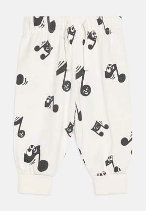 Pantalons pour enfants blancs avec des notes de musique noires comportant des visages souriants imprimés partout, taille élastique et chevilles resserrées.