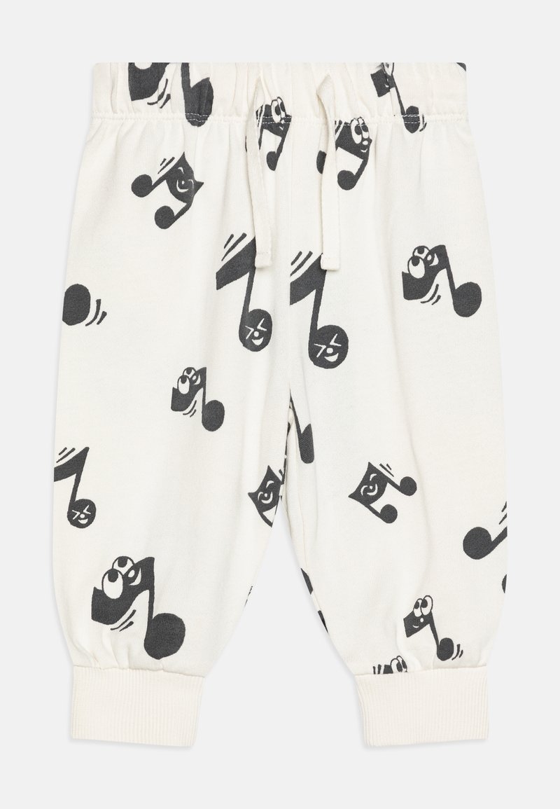 Pantalons pour enfants blancs avec des notes de musique noires comportant des visages souriants imprimés partout, taille élastique et chevilles resserrées.