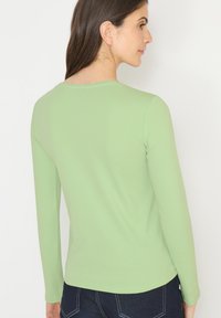 Long-sleeve top in light green cotton blend, featuring a crew neckline and smooth texture. The back view shows fitted sleeves and a curved hem.