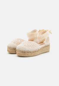 Lace espadrille shoes in light beige, featuring intricate embroidery, a woven jute sole, and satin ribbon ankle ties. Flat heel design.