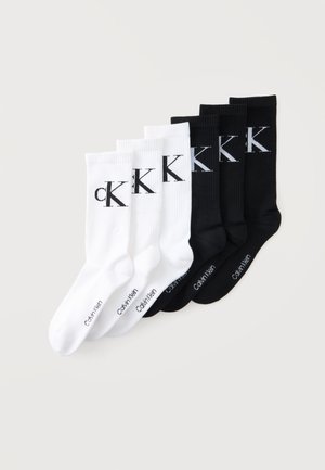 Trzy pary białych skarpet i trzy pary czarnych skarpet z dużymi logo CK i napisem Calvin Klein na podeszwach, starannie ułożone.