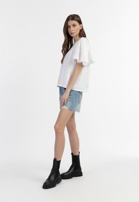 Hvid tekstureret bluse med flæser ved ærmerne, parret med lyseblå denim shorts og sorte læder ankelstøvler med en kraftig sål.