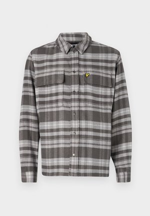 Chemise à carreaux grise avec deux poches poitrine, fermeture à boutons et accent de logo jaune. Le tissu a une finition texturée et un design de col classique.