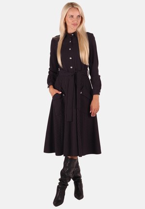 Schwarz- und grau gestreiftes langes Kleid mit durchgehender Knopfleiste, tailliertem Gürtel, zwei Seitentaschen und langen Ärmeln, kombiniert mit kniehohen schwarzen Stiefeln.