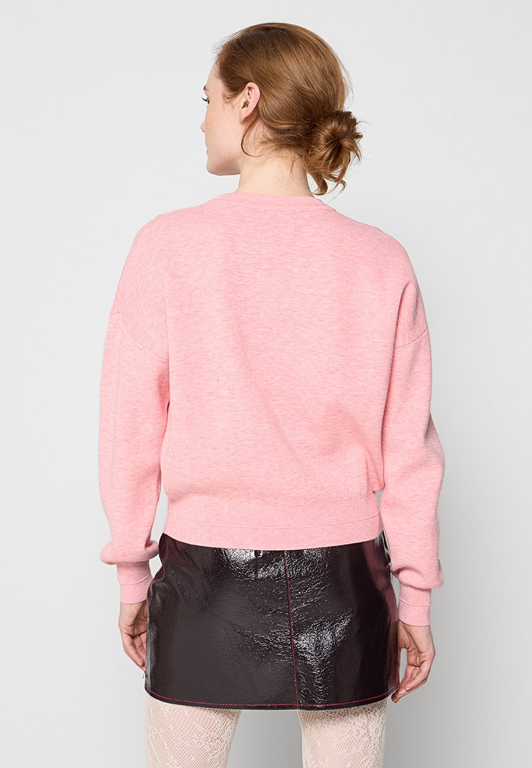 Roze sweatshirt met een ronde halslijn en verlaagde schouders, gecombineerd met een zwarte lakleren minirok met rode stiksels.