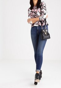 Top floreale a maniche lunghe in rosa e nero, abbinato a jeans skinny blu scuro. Borsa nera con dettaglio a catena e scarpe con tacco largo.