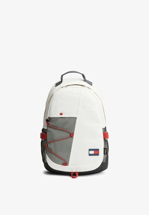 Sac à dos blanc et noir avec des touches rouges, poche avant en mesh, sangles latérales réglables et un écusson logo Tommy Jeans sur la partie basse avant.