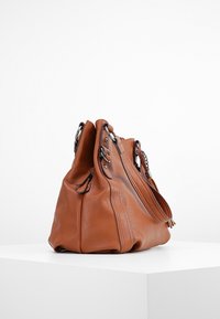 Bruine leren handtas met een gestructureerde vorm, voorzien van twee handvatten, een ritssluiting en decoratieve hardware-accenten.