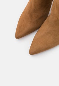 Ein Paar braune Wildleder-Schuhe mit spitzem Vorderteil auf einem weißen Hintergrund, der die Textur und das elegante Design des Schuhwerks hervorhebt.
