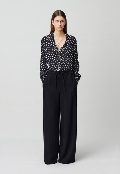 Blusa nera floreale con bottone e colletto, abbinata a pantaloni neri a gamba larga con cintura regolabile.