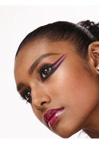 Primo piano di un volto con eyeliner nero e accenti rosa, ciglia lunghe e labbra rosa scure e lucide. Texture della pelle liscia.