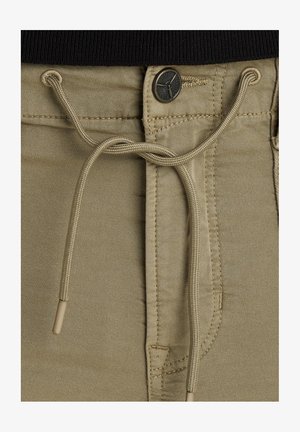 Joggers in tessuto beige con vita regolabile tramite coulisse, chiusura a bottone metallico e dettagli di cucitura a contrasto. Texture liscia e design casual.
