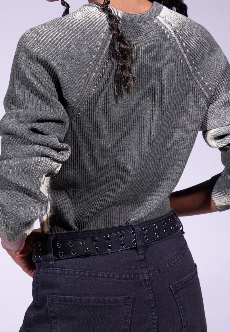 Gestreifter grauer Pullover mit strukturierter Oberfläche und umgeschlagenen Ärmeln, kombiniert mit dunklen Hosen und einem Gürtel mit Metallösen.