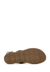Suela de goma marrón con surcos horizontales, que presenta una superficie plana. Tiras de sandalia en negro con acentos metálicos sujetas con hebillas.
