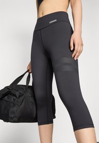 Mustad kapri legginsid laia vööga, külgedel punktprindiga aktsentidega ja siledast, venivast kangast. Hoitakse musta spordikotti.