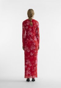 Langermet rød kjole med blomsterprint i rosa, tettsittende silhuett, gjennomsiktig stoff og rett kant. Kombinert med svarte hæler.