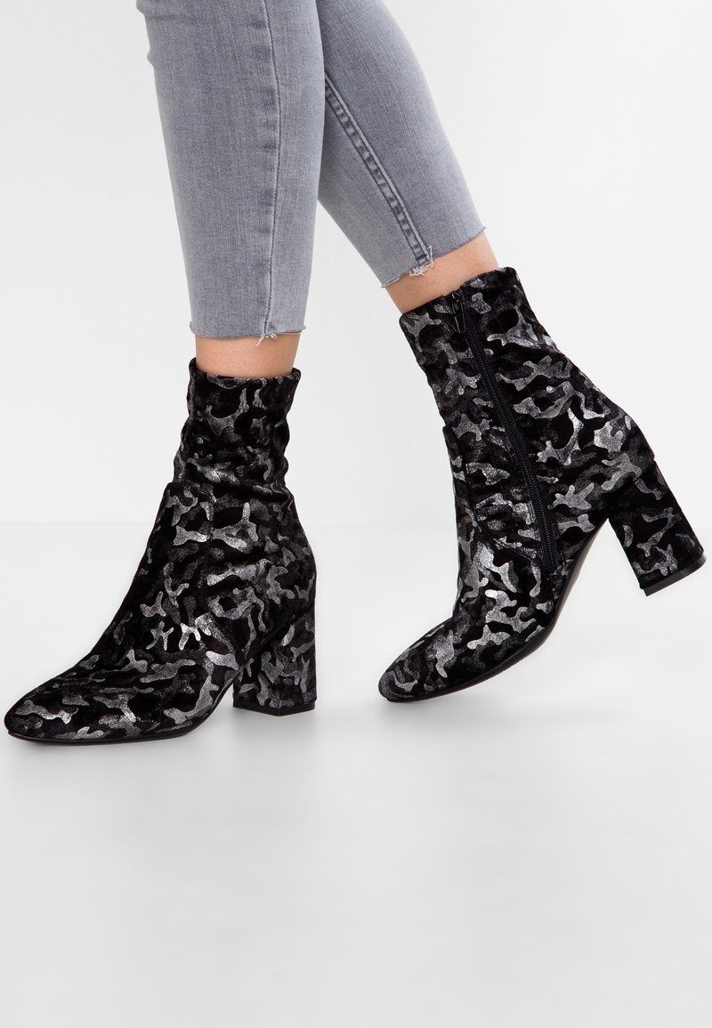 Bottines en velours noir avec un motif camouflage argent texturé, bouts pointus et talons épais, dotées d'une fermeture éclair latérale.