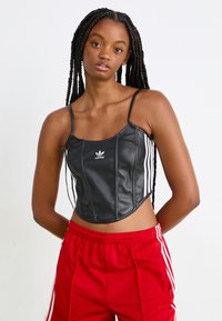 Top cropped em pele sintética preta com alças finas, featuring a marca Adidas em branco e riscas verticais brancas ao longo das laterais.