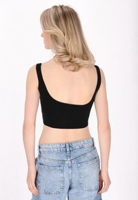 Černý zkrácený top s širokými ramínky a nízkým výstřihem na zádech, kombinovaný s vysokými světle modrými denimmovými šortkami s kapsami na zadní straně.