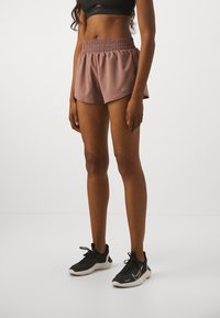 Bruna sportshorts med elastisk midjeband och innertyg, tillsammans med svarta träningsskor med vita detaljer och texturerat material.