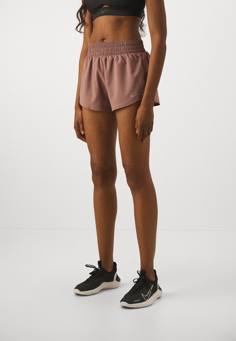 Bruna sportshorts med elastisk midjeband och innertyg, tillsammans med svarta träningsskor med vita detaljer och texturerat material.