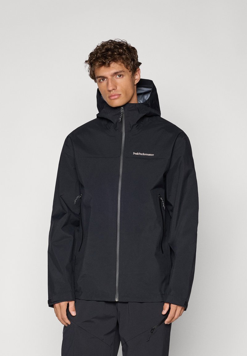 Veste imperméable noire avec fermeture éclair à l'avant, capuche réglable et deux poches latérales zippées. Présente un logo sur la poitrine et une texture lisse.