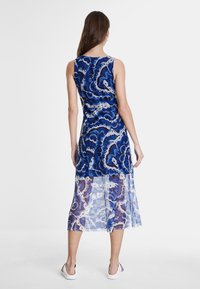 Robe sans manches bleue avec un motif en spirale détaillé, tissu léger et transparent en bas, et silhouette droite.