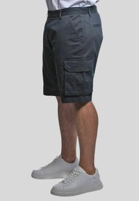 Pantaloni cargo grigi scuri realizzati in misto cotone, con tasche laterali e una vestibilità comoda. Abbinati a sneakers bianche per un look casual.