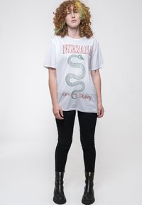White cotton t-shirt with green snake graphic and red text "NIRVANA" and "SERVE THE SERVANTS," paired with black skinny jeans and black boots.