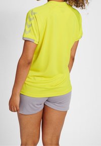 Gul sporttröja med grå detaljer, korta ärmar och chevronmönster på axlarna, ihop med grå shorts, slät tygkvalitet.