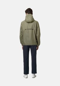 Giacca verde oliva con cappuccio, vestibilità comoda, polsini elasticizzati e dettagli sul dorso. Abbinata a pantaloni blu marino e scarpe bianche.