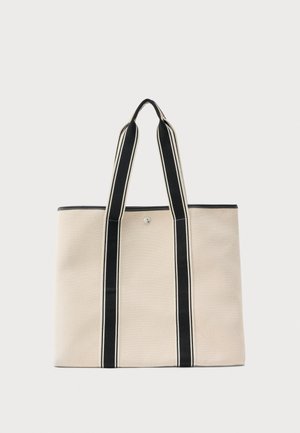 Μπεζ τσάντα tote από καμβά με δύο μακριές μαύρες και λευκές ριγέ λαβές και κούμπωμα με κουμπί στη μέση στην κορυφή.