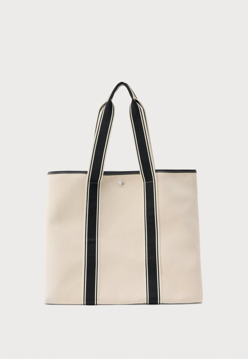 Μπεζ τσάντα tote από καμβά με δύο μακριές μαύρες και λευκές ριγέ λαβές και κούμπωμα με κουμπί στη μέση στην κορυφή.