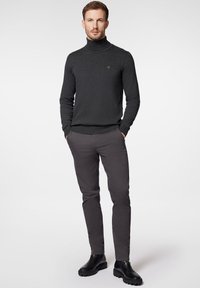 Ciemnoszary sweter golf o dopasowanym kroju, w zestawie z szarymi spodniami o slim fit i czarnymi botkami za kostkę. Gładka faktura, minimalne logo.