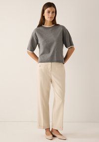 Grauer Kurzarm-Pullover mit kontrastierendem weißen Besatz, kombiniert mit cremefarbenen, maßgeschneiderten Hosen mit Fronttaschen und Knöpfen.